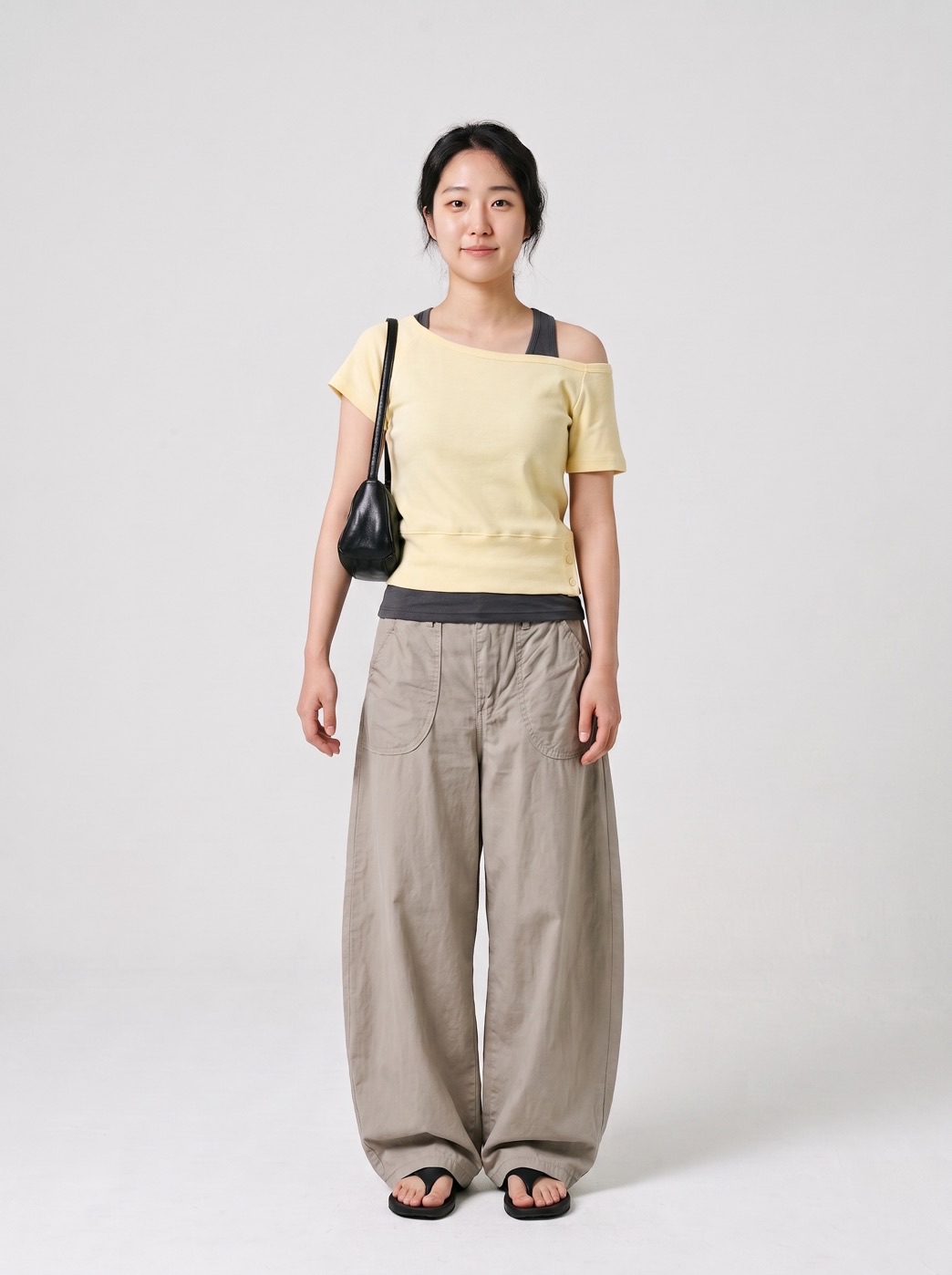 A Style Sketch outfit suggestion: a butter-yellow one-shoulder top layered over a charcoal tank, with taupe wide-leg trousers, black sandals and a small black shoulder bag.